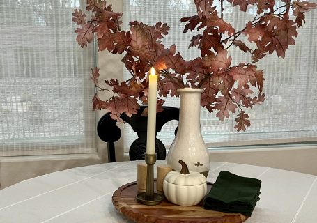 Fall dining table decorated with warm neutral colors, wood, candles, and dark green napkins