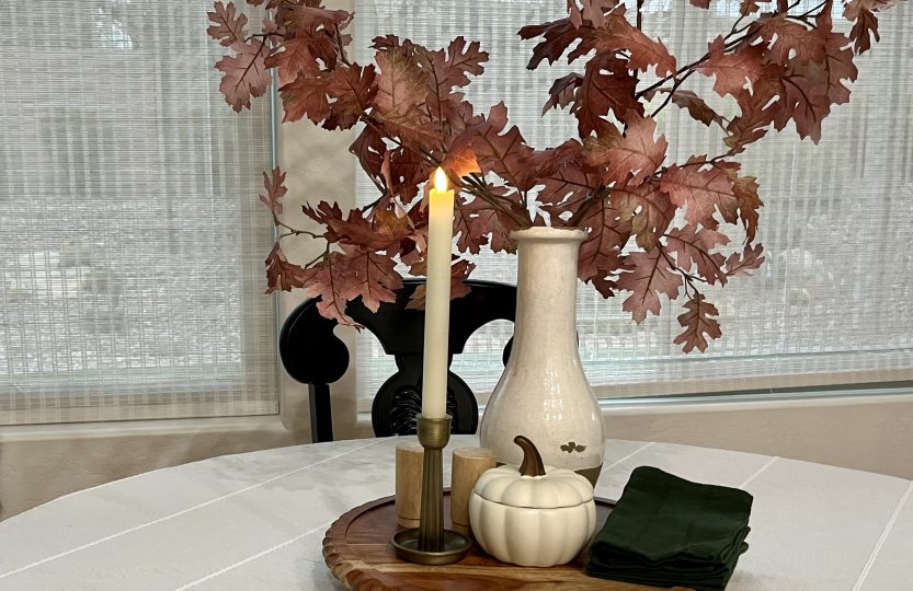 Fall dining table decorated with warm neutral colors, wood, candles, and dark green napkins