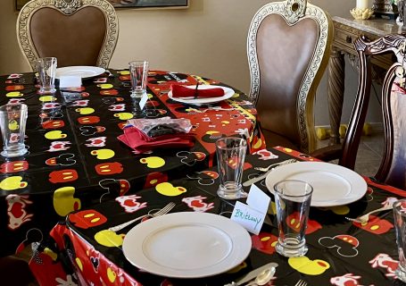 Mickey Mouse birthday party table decorated with themed tablecloth, red napkins, white plates and Mickey Mouse balloons