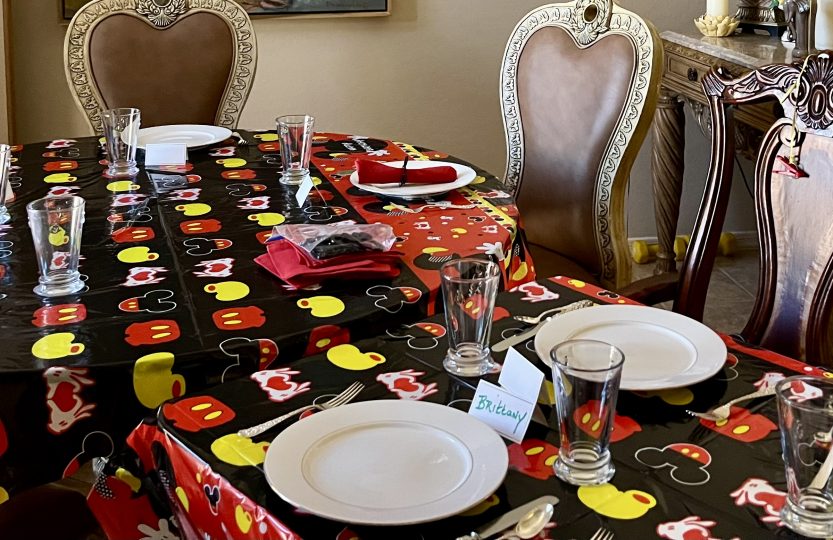 Mickey Mouse birthday party table decorated with themed tablecloth, red napkins, white plates and Mickey Mouse balloons