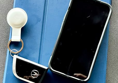Bluetooth tracker attached to car keys beside an iPhone and iPad.