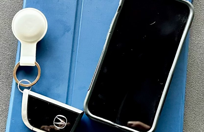 Bluetooth tracker attached to car keys beside an iPhone and iPad.